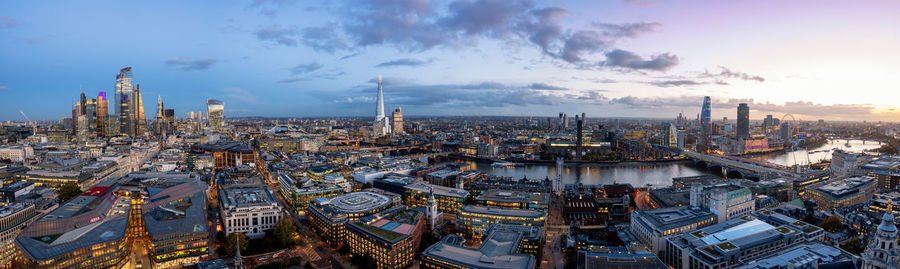 Aerial view of illuminated city by river against sky during dusk