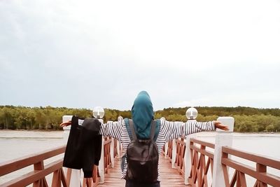 Rear view of woman with arms outstretched standing on pier over lake