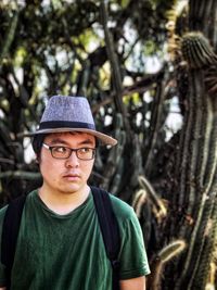 Portrait of young man wearing hat against forest of tall cacti.