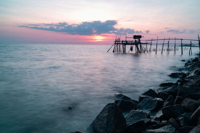 Wooden jetty at the rocky seaside during sunset.