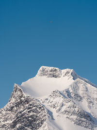 Low angle view of snowcapped mountain against clear blue sky