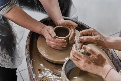 Hands of senior woman and girl sculpting clay vase on potter's wheel at pottery training lesson.