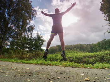 Rear view of man jumping on land against sky