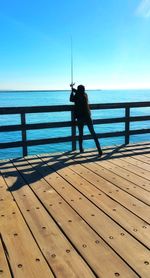 Man standing on railing by sea against sky