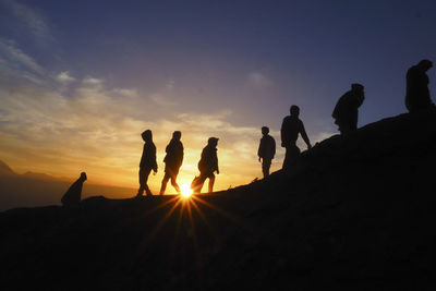 Silhouette people hiking on mountain against sky during sunset