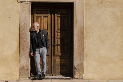 Man in black suit standing in front of wooden door against wall