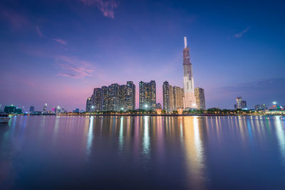 Buildings by river against sky at night