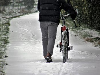 Low section of man with bicycle walking on snow covered field