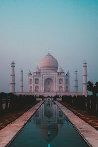 Pond leading towards taj mahal in city against sky