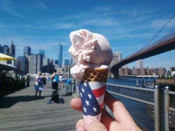 Cropped hand holding ice cream cone on brooklyn bridge against sky