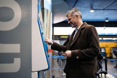 Side view of man standing near ticket vending machine