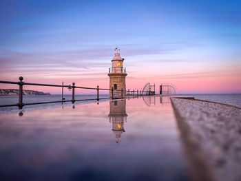 Lighthouse by sea against sky during sunset