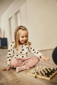 Curious girl sitting cross-legged pointing at chess board