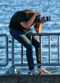 Side view of man photographing against railing