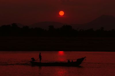 Silhouette man in boat on sea against sky at sunset