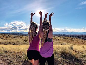 Rear view of female friends gesturing while standing on field against sky