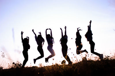 Silhouette people jumping on field against clear sky