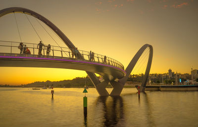 People on bridge over river against sky during sunset