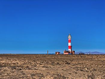 Lighthouse on street amidst buildings against clear blue sky