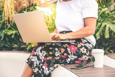 Midsection of woman using laptop while sitting against plants