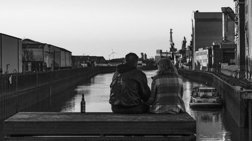 Rear view of people on bridge over river against sky in city