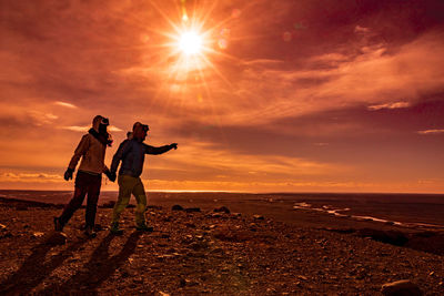 Friends standing on beach against sky during sunset