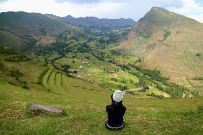 Rear view of girl sitting on grass against mountains and sky