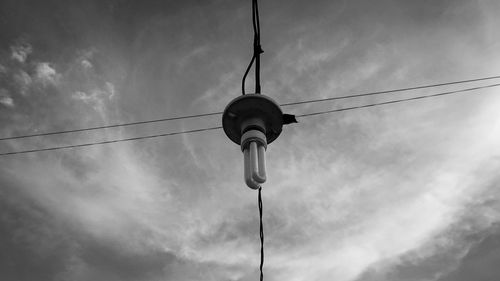 Low angle view of light bulb hanging on cable against sky