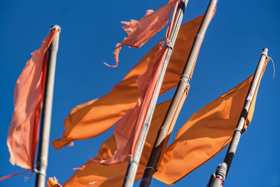 Low angle view of orange flags waving against clear blue sky