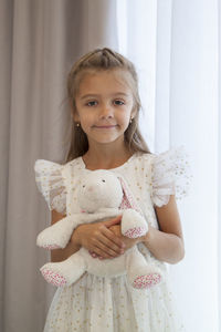 Portrait of smiling girl holding toy standing against wall at home