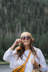 Portrait of young woman wearing sunglasses while standing against trees