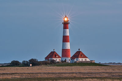 Lighthouse on field by building against clear sky