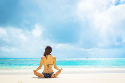 Rear view of woman standing at beach against sky