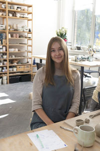 Portrait of the beautiful young woman in a work apron. professional potter sculpts a mug out of clay