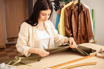 Black haired seamstress in atelier, portrait at work. table with fabric and sewing tools, indoors. 