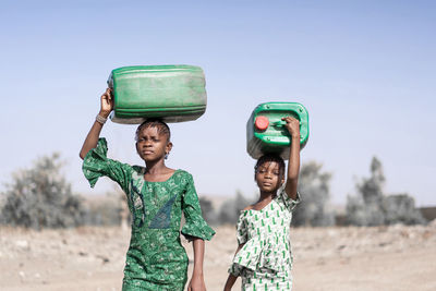 Portrait of girls carrying containers while walking on land