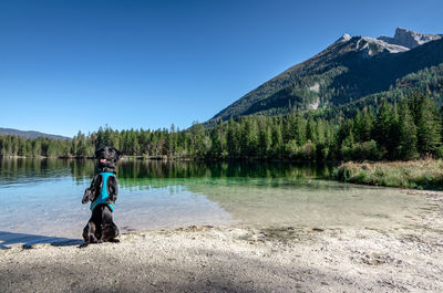 Man sitting by lake against clear sky