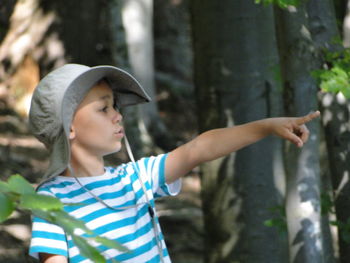 Side view of boy pointing while standing in forest