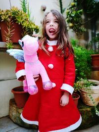 Cheerful girl holding unicorn toy while standing against potted plants in yard