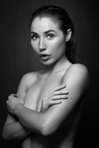 Portrait of shirtless young woman with arms crossed standing against black background