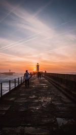 People by lighthouse amidst sea against sky during sunset
