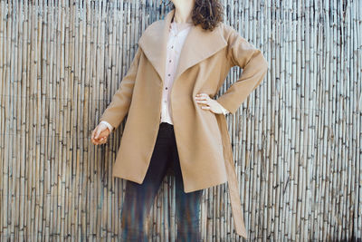 Midsection of woman wearing overcoat by bamboo wall