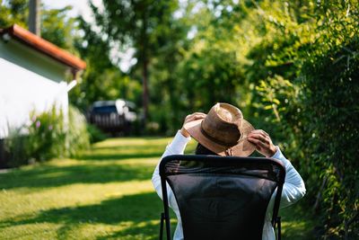 Rear view of man with sun hat sitting on chair in the garden at home