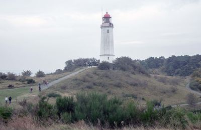 Lighthouse on field by building against sky