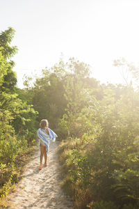 Rear view of girl with towel walking on footpath amidst plants