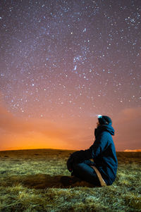 Rear view of woman sitting on field against sky at night