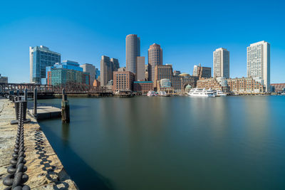 River by city buildings against clear blue sky