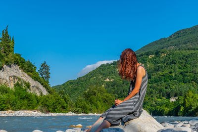 Woman sitting by mountain against blue sky