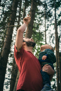 Low angle view of father carrying son while standing in forest