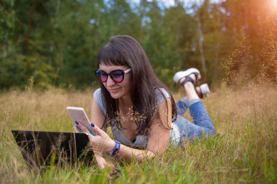 Smiling woman using mobile phone lying on grass